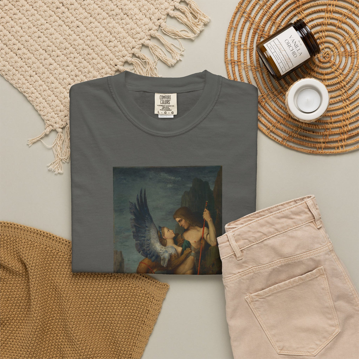 Old Heaven The Riddle tee in Pepper folded flat with Moreau's Oedipus and the Sphinx print, styled with a candle and woven textiles